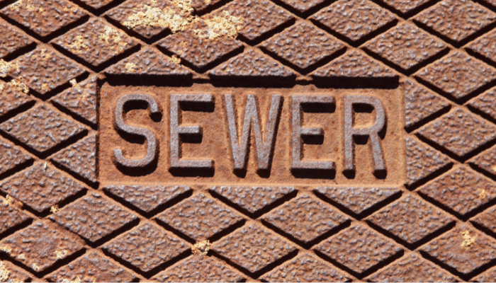 Close-up of a rusted metal sewer cover with raised diamond pattern and the word SEWER embossed in the center.